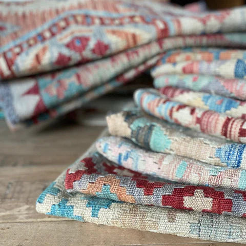 a selection of woven antique kilim rugs and runners displayed in a pile on a stripped wood floor