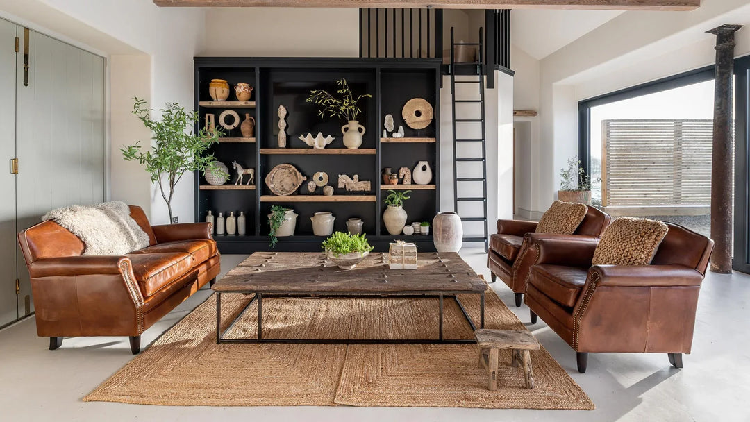 An extra large antique door coffee table with vintage leather club chairs and a collection of decorative antiques