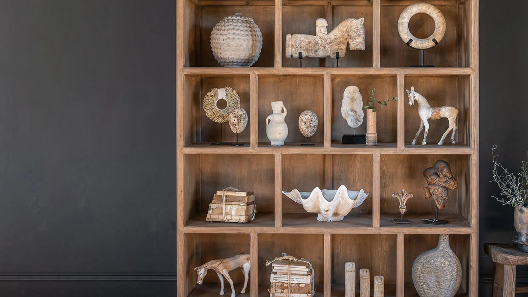 A modern rustic interior room with dark wall and pale reclaimed shelving displaying a collection of decorative antiques. 