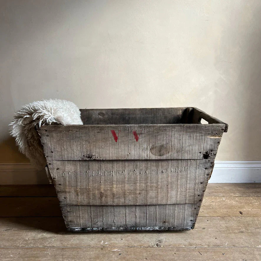 a rustic monogrammed antique champagne crate displayed on a stripped pine floor and filled with sumptuous sheepskin throws