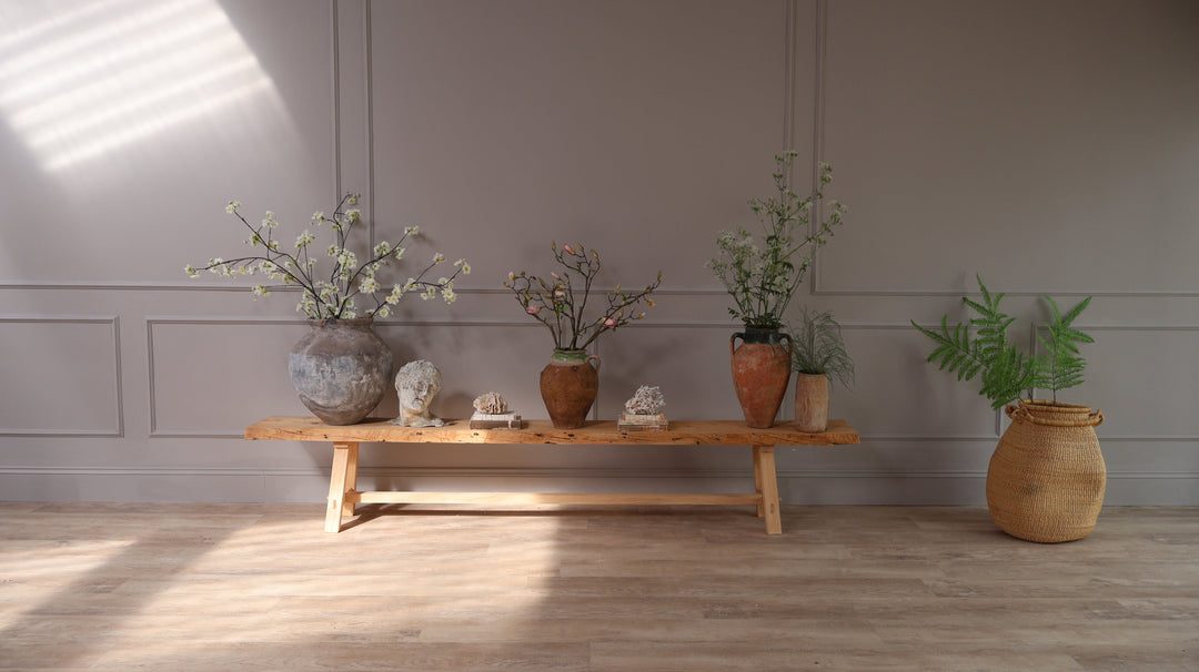 Beautiful Flowers and Foliage products displayed in Vintage and antique Urns on a rustic wooden bench, displayed against a grey panelled wall in a period home.