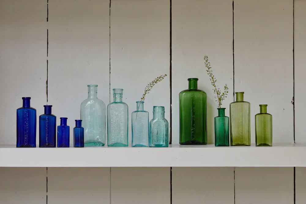 a collection of antique glass apothecary bottles in shades of blues and greens displayed together on a shelf