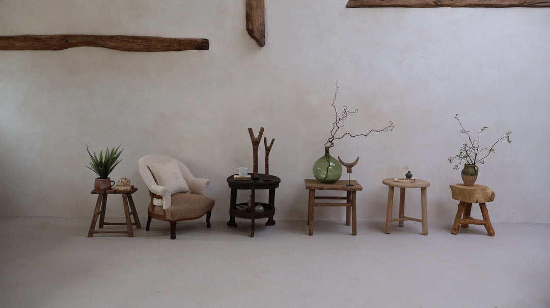 A collection of rustic and antique side tables from around the world displaying a selection of antique glassware and tribal african antiques