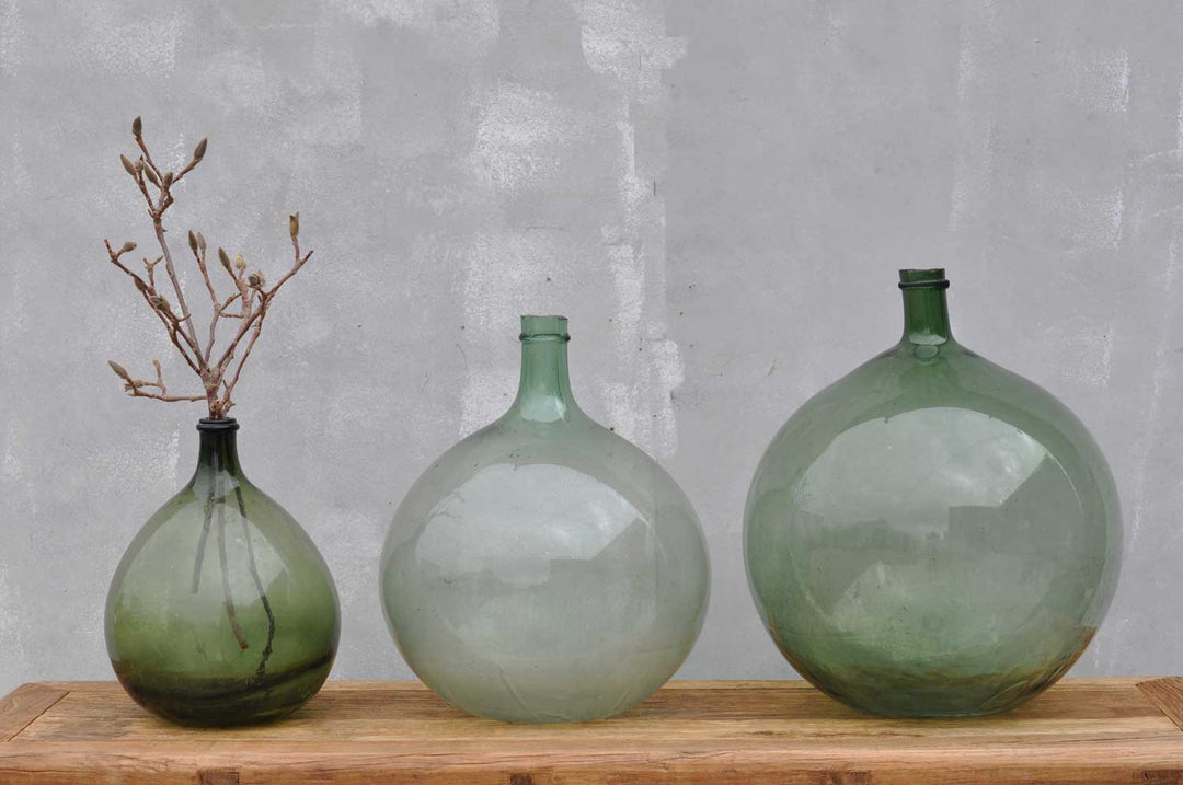 a collection of green glass antique vases or carboys in a line on a table top