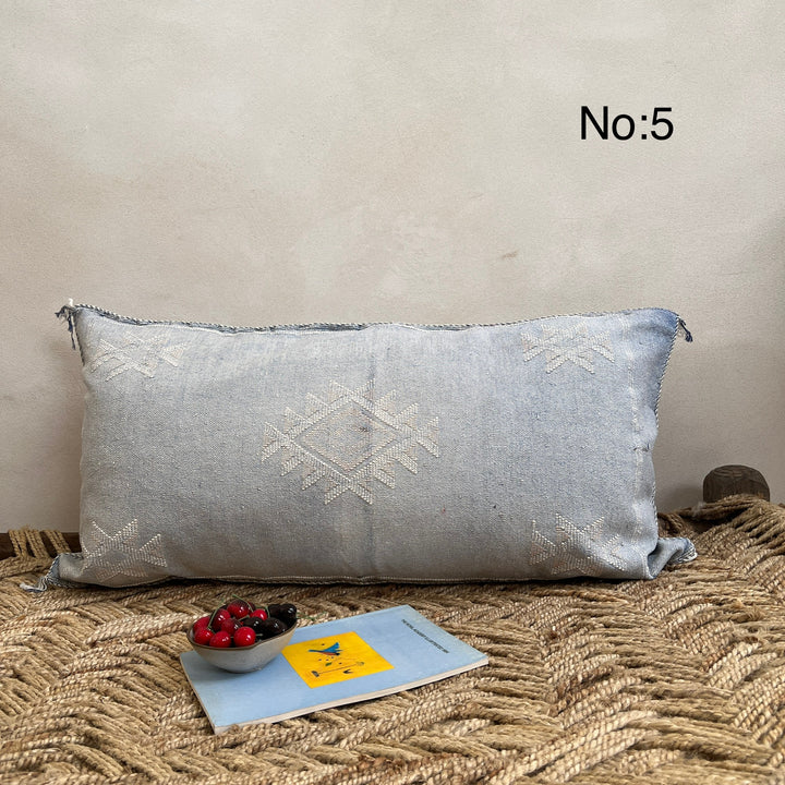 Cactus Silk Cushion Gray textured pillow on a textured surface with a small bowl of berries and a book.