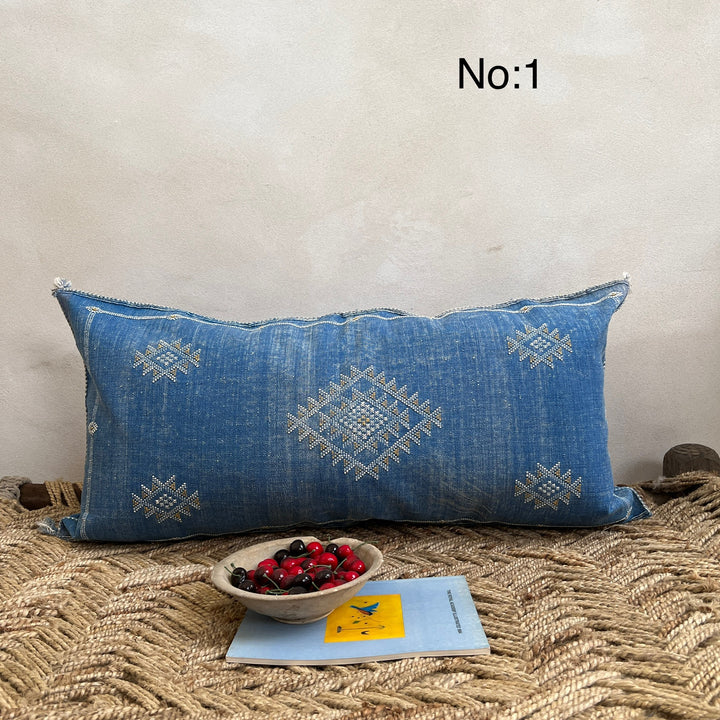 Blue embroidered pillow on a textured surface with a bowl of berries and a book.