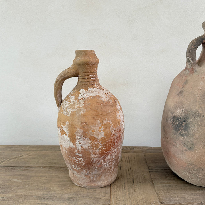 Two rustic clay jugs on a wooden surface with a white wall background