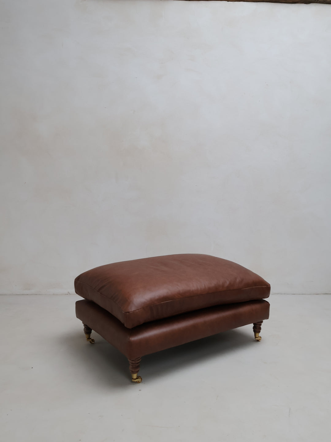 BROWN LEATHE OTTOMAN IN A STUDIO SETTING
