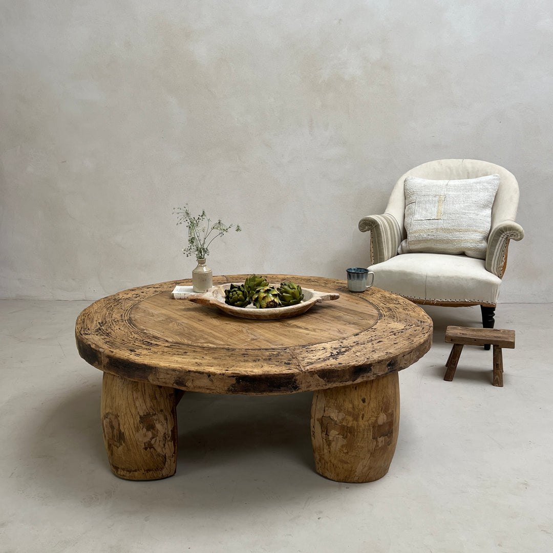 Round wooden coffee table with a chair and decorative items in a minimalistic room.