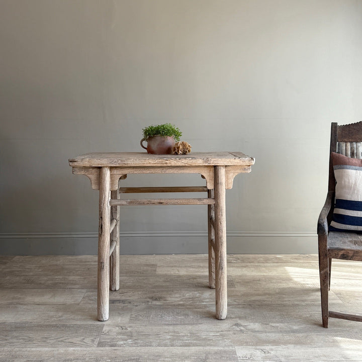 Wooden table with a plant and chair against a plain wall