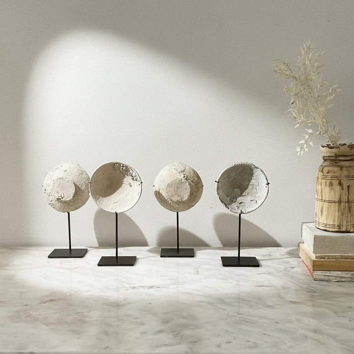 Four decorative moon-like objects on stands against a neutral background