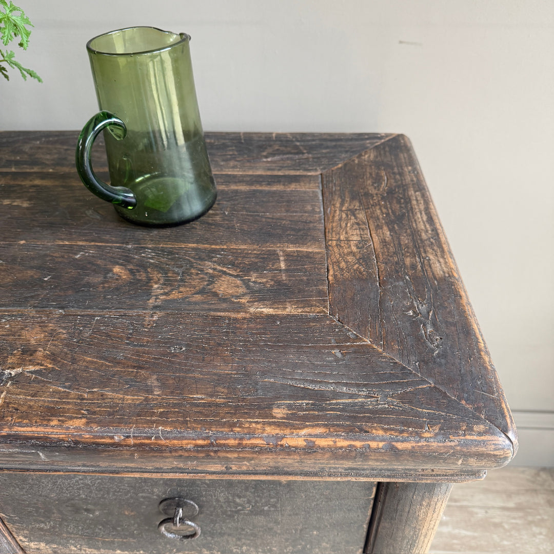 A translucent dark green glass mug with a handle, resting on the corner of a rustic dark brown wooden table.