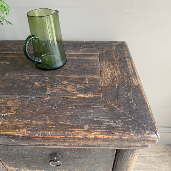 A translucent dark green glass mug with a handle, resting on the corner of a rustic dark brown wooden table.