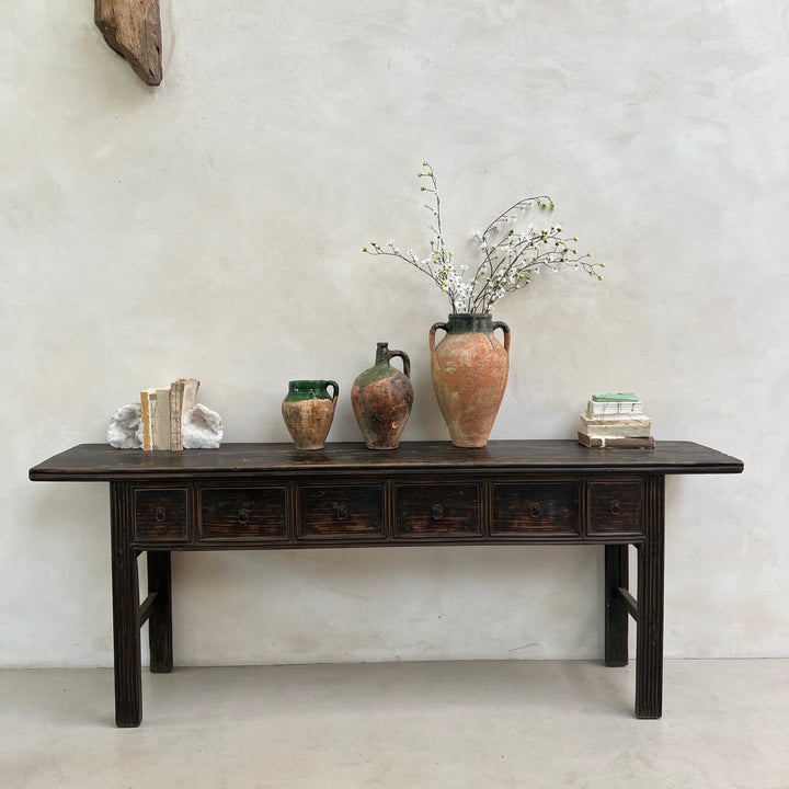 Vintage wooden table with decorative vases and books against a plain wall.