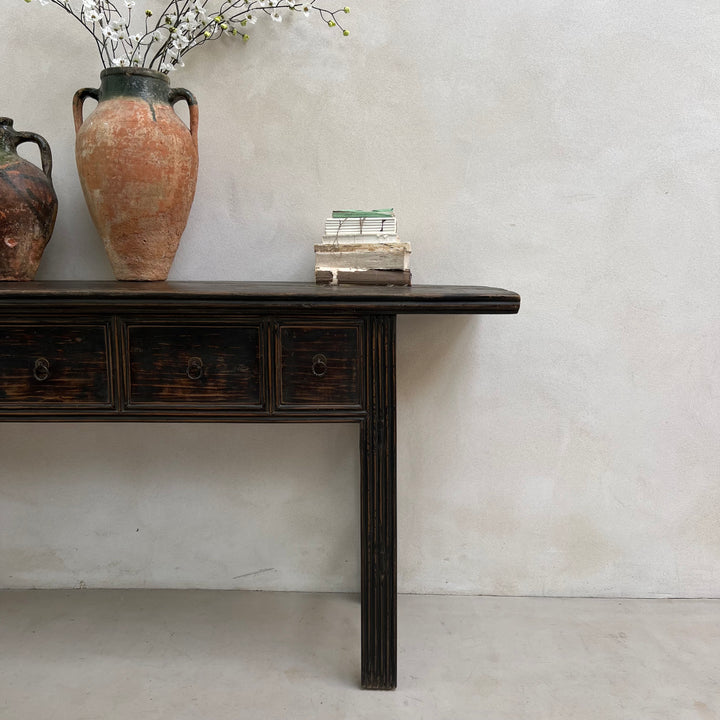 Wooden console table with decorative items against a plain wall