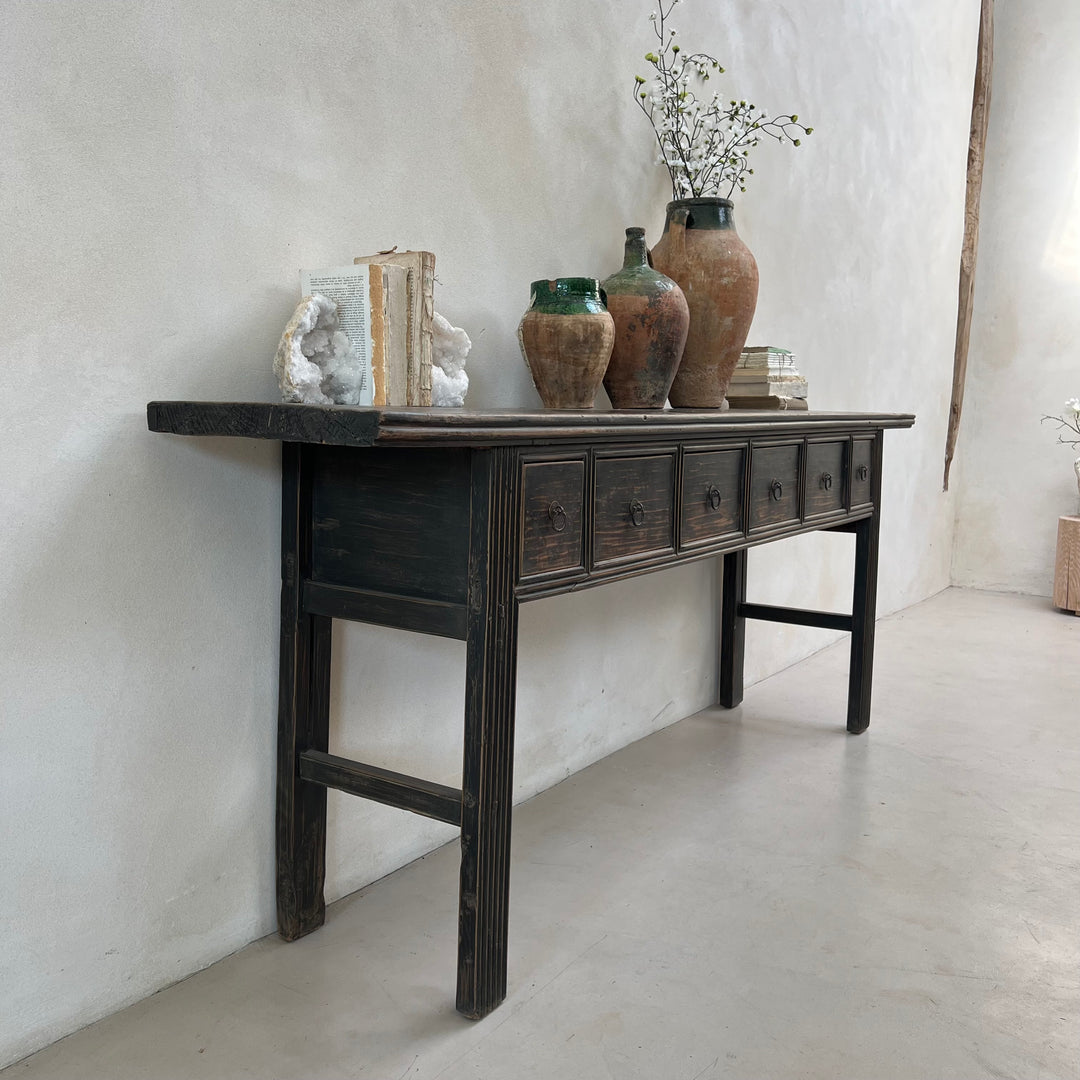 Vintage wooden console table with decorative items against a white wall.