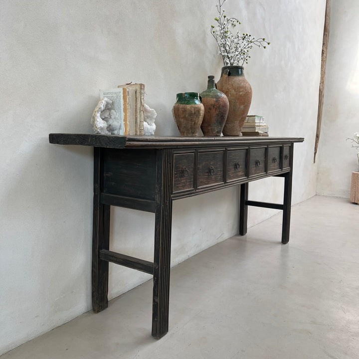 Vintage wooden console table with decorative items against a white wall.