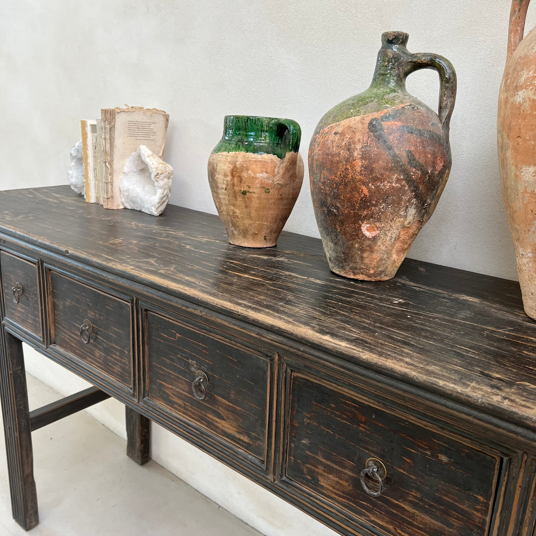 Vintage wooden sideboard with rustic ceramic jars and books against a white wall.