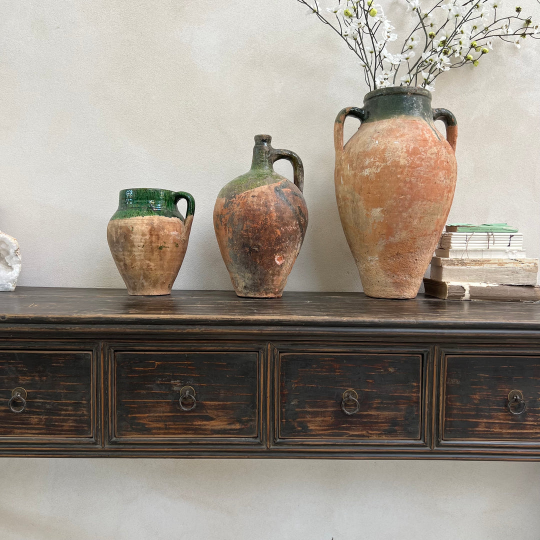 Three rustic ceramic jars on a wooden dresser against a light wall.