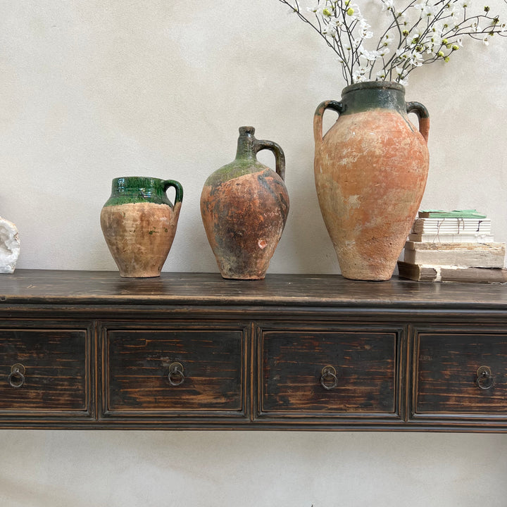 Three rustic ceramic jars on a wooden dresser against a light wall.