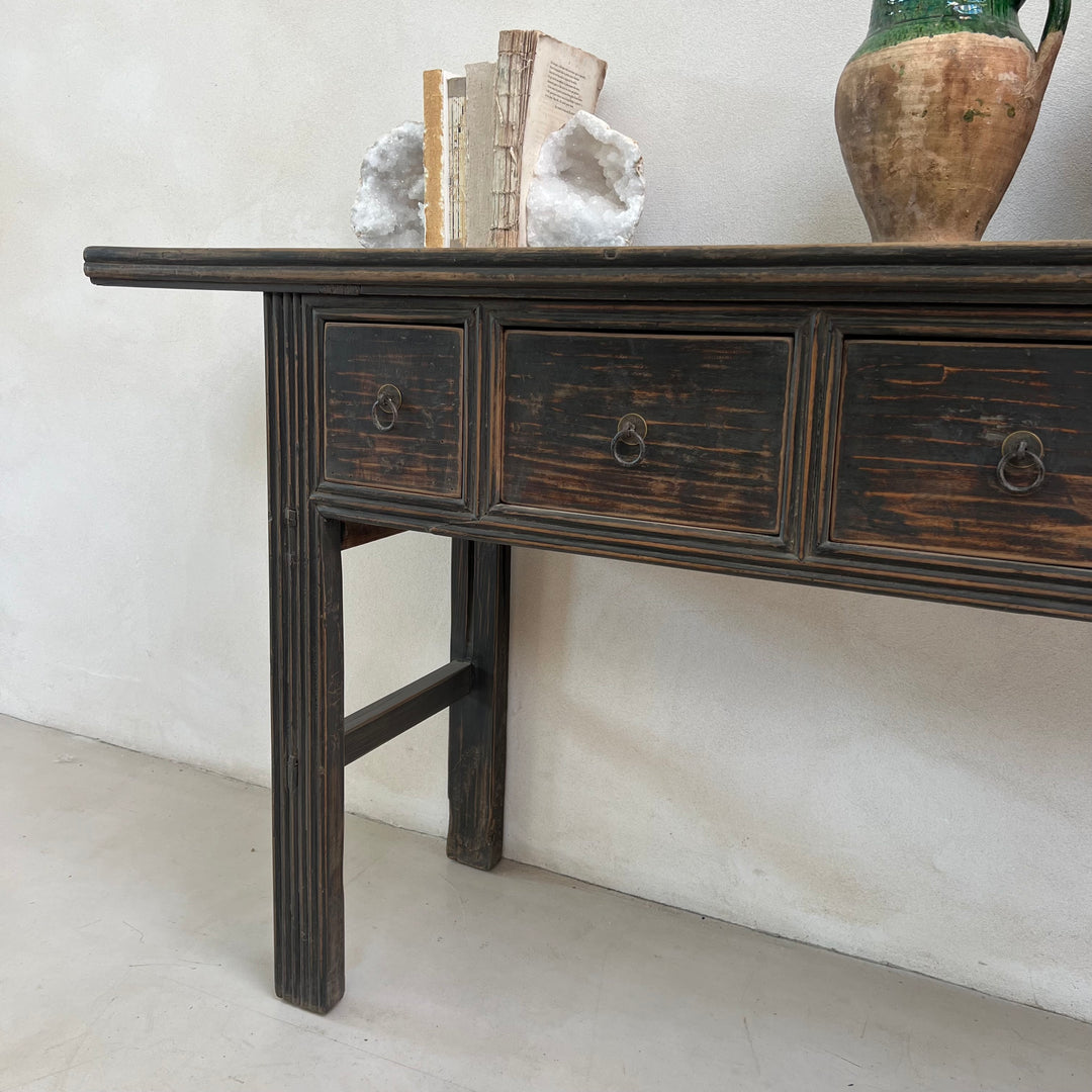 Wooden console table with three drawers against a white wall.