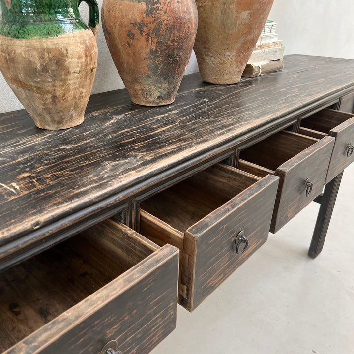 Wooden sideboard with open drawers and rustic vases on a white floor.