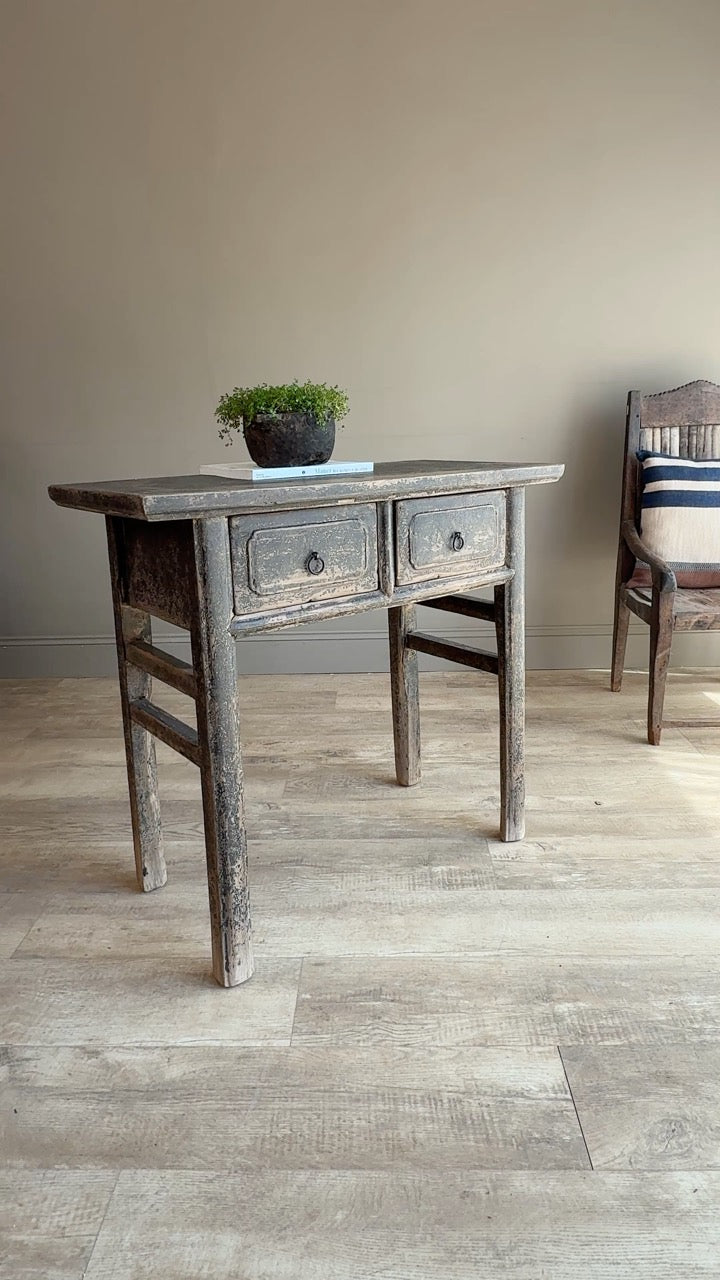 Wooden desk with two drawers in a room with a chair and plant.