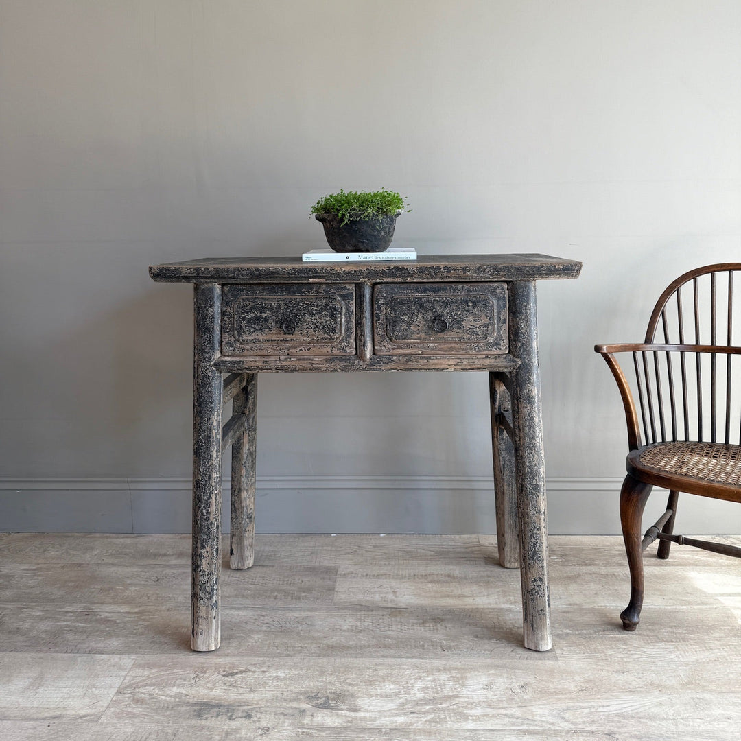 Vintage wooden table with a plant on a light wooden floor against a plain wall.