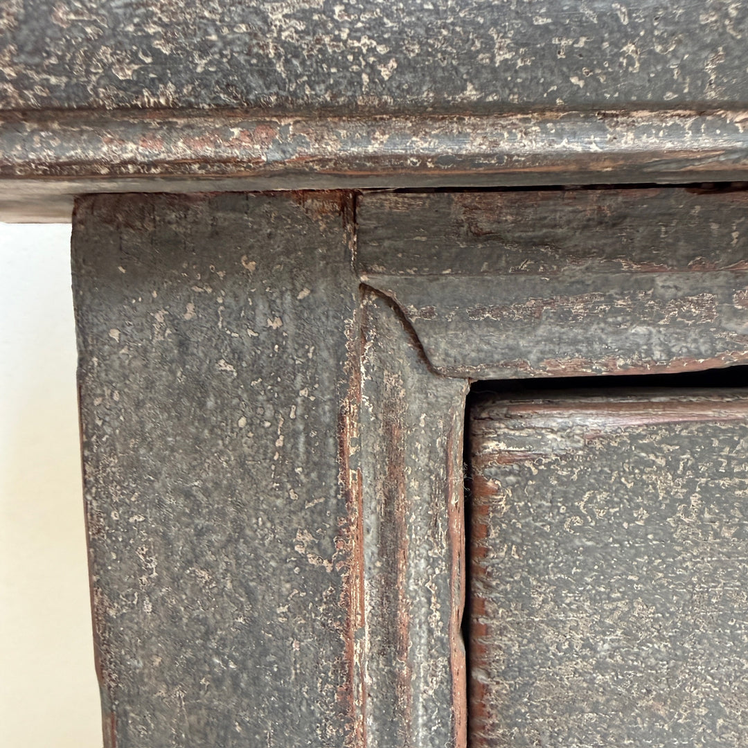 Close-up detail of a distressed dark gray wooden cabinet corner with peeling weathered paint and visible wood grain.