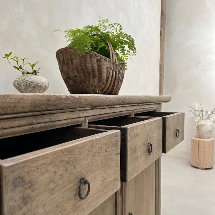 Wooden sideboard with open drawers and decorative plants in a home setting