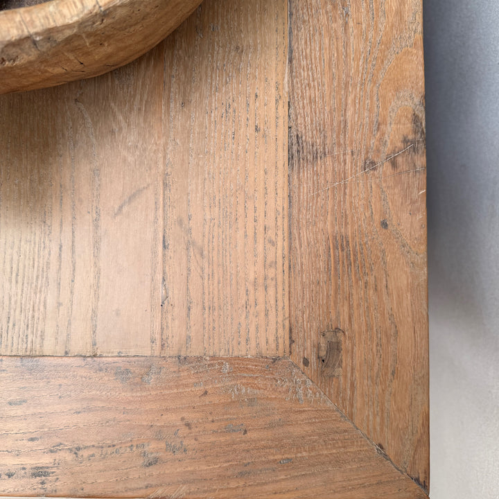 Close-up of a rustic wooden surface showing natural oak grain, with a curved wooden object partially visible at the top left and a neutral gray background on the right.