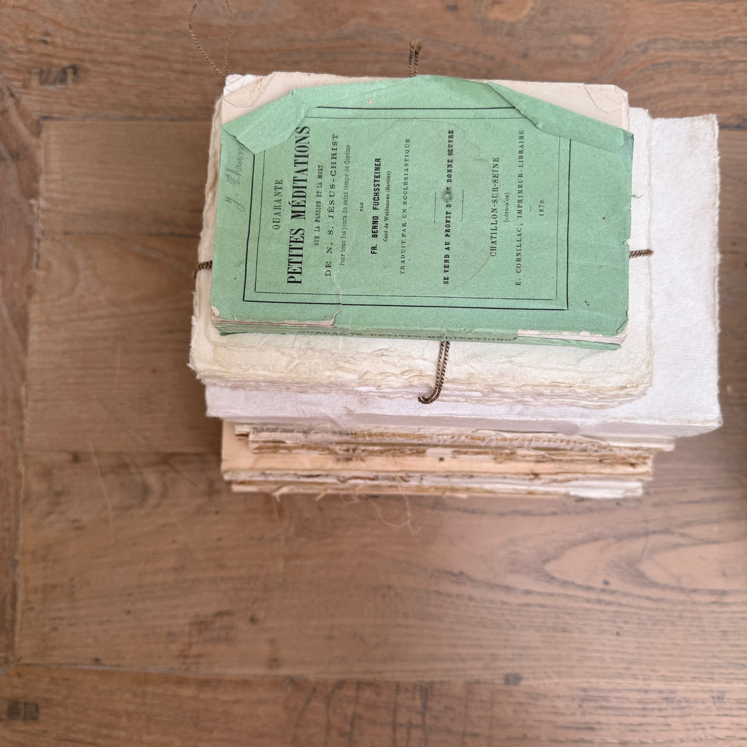 A stack of old, worn paper notebooks or books on a wooden tabletop, with a light green vintage booklet on top reading &