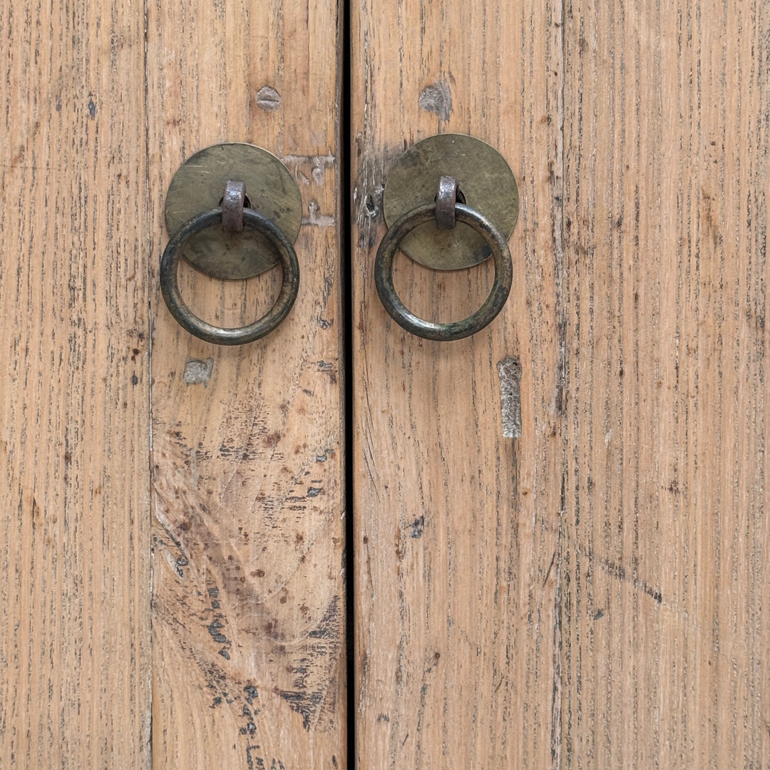 Two round metal ring door knobs with circular backplates mounted on weathered light brown wooden doors.