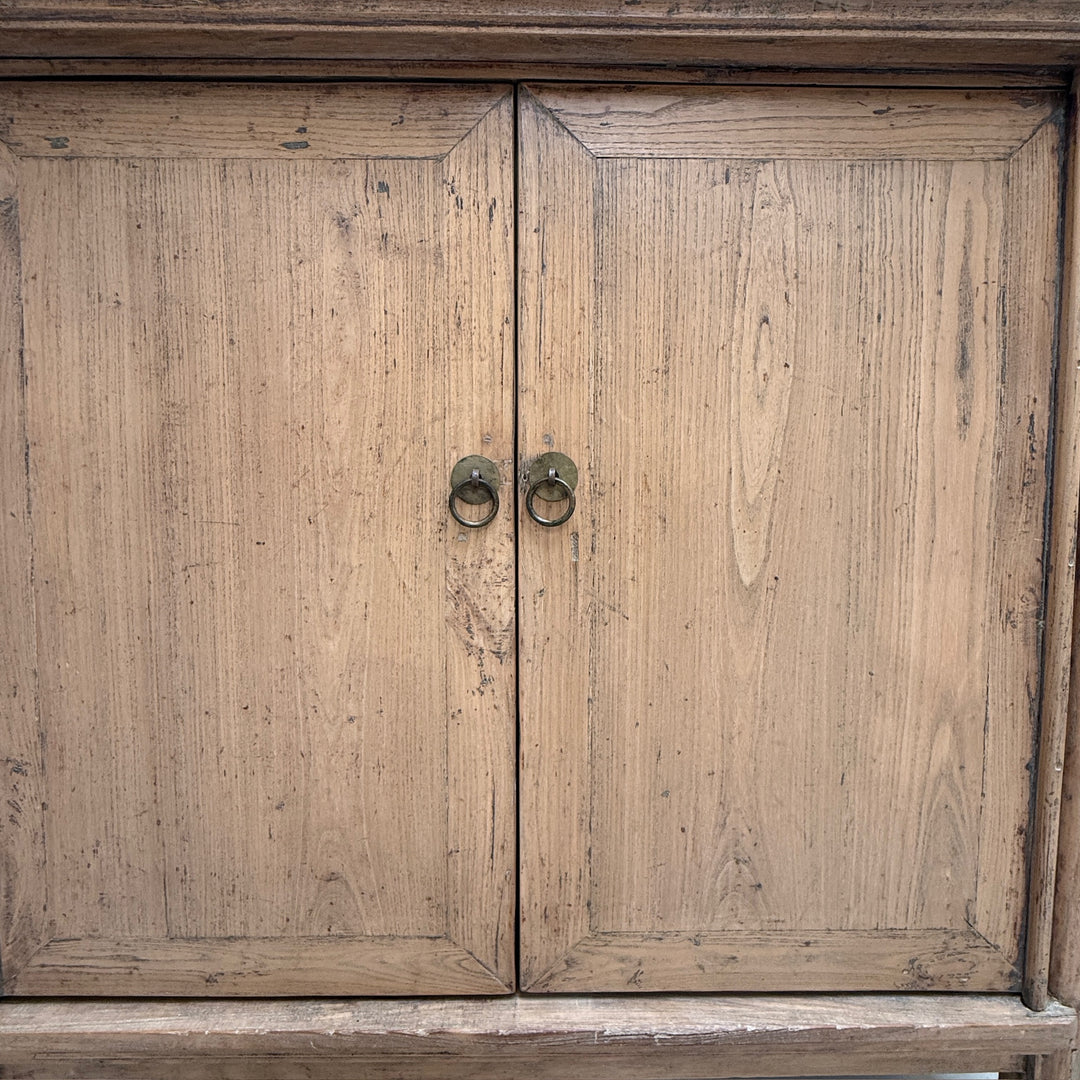 A close-up of a rustic wooden cabinet with two doors and round metal ring pulls, showing visible wood grain and distressing.