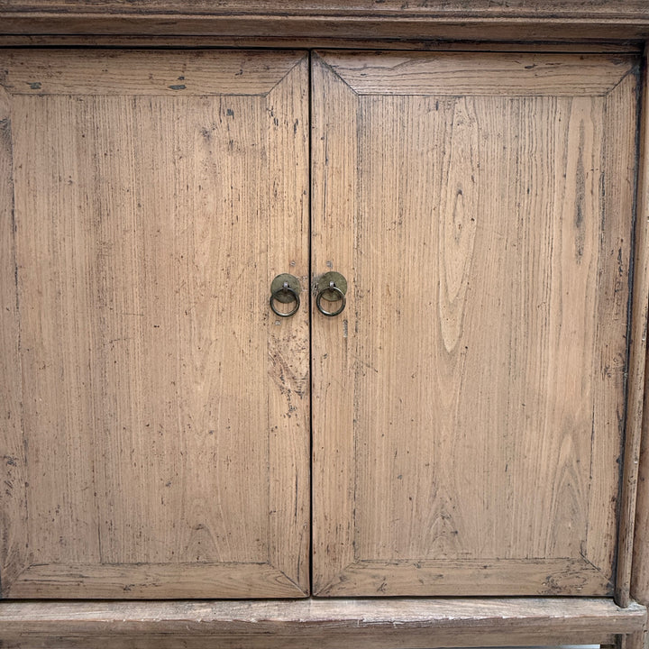 A close-up of a rustic wooden cabinet with two doors and round metal ring pulls, showing visible wood grain and distressing.