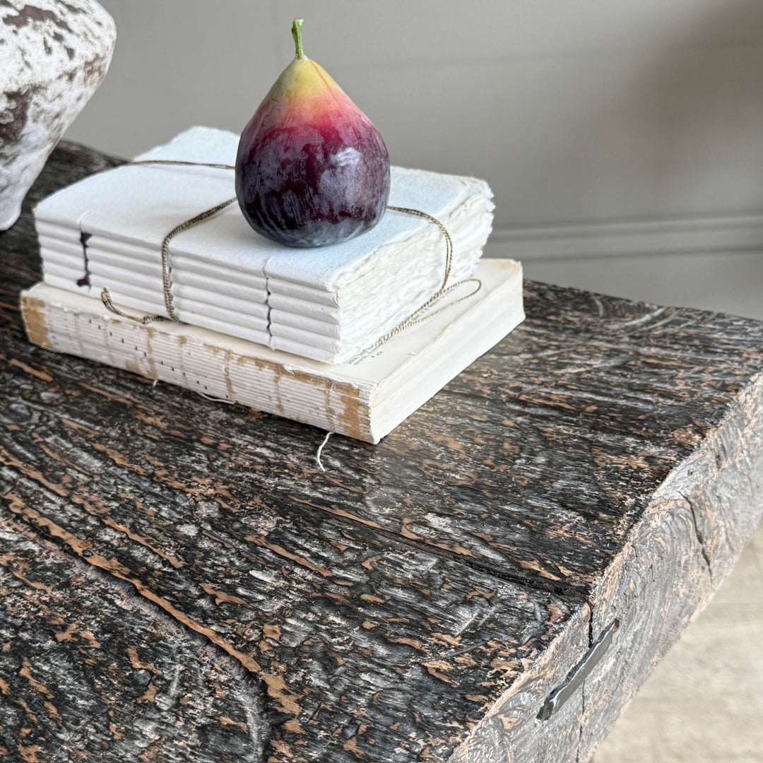 A stack of white ceramic coasters tied with twine, placed on a rustic dark wood table, with a fig fruit on top.