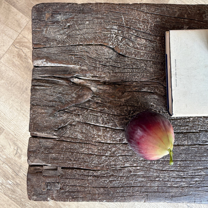 A rustic dark brown wooden plank surface with a whole fig and a closed book placed on it, photographed from above on a light wood floor.