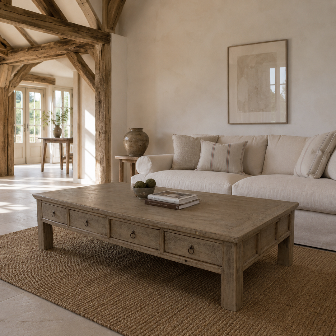 A rustic light brown wooden coffee table with three drawers and round metal knobs, styled in a bright, modern bohemian living room with a cream sofa and a woven jute rug.