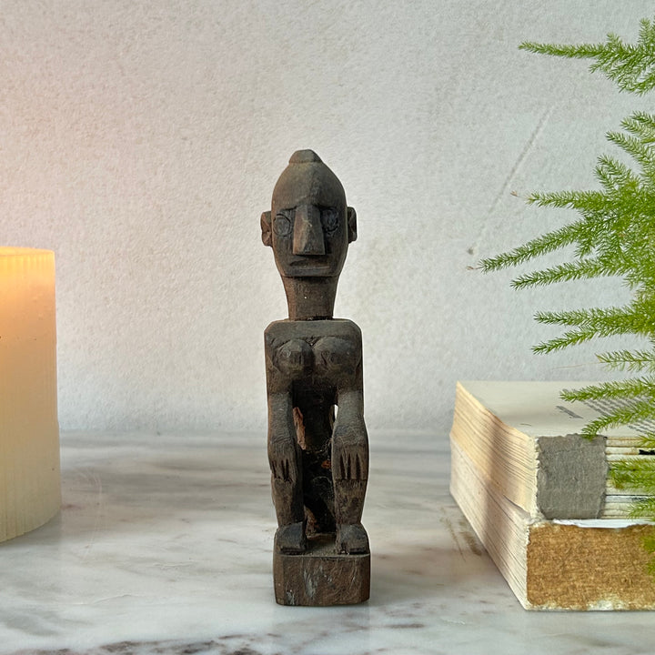 Wooden figurine on a marble surface with a candle and plant in the background