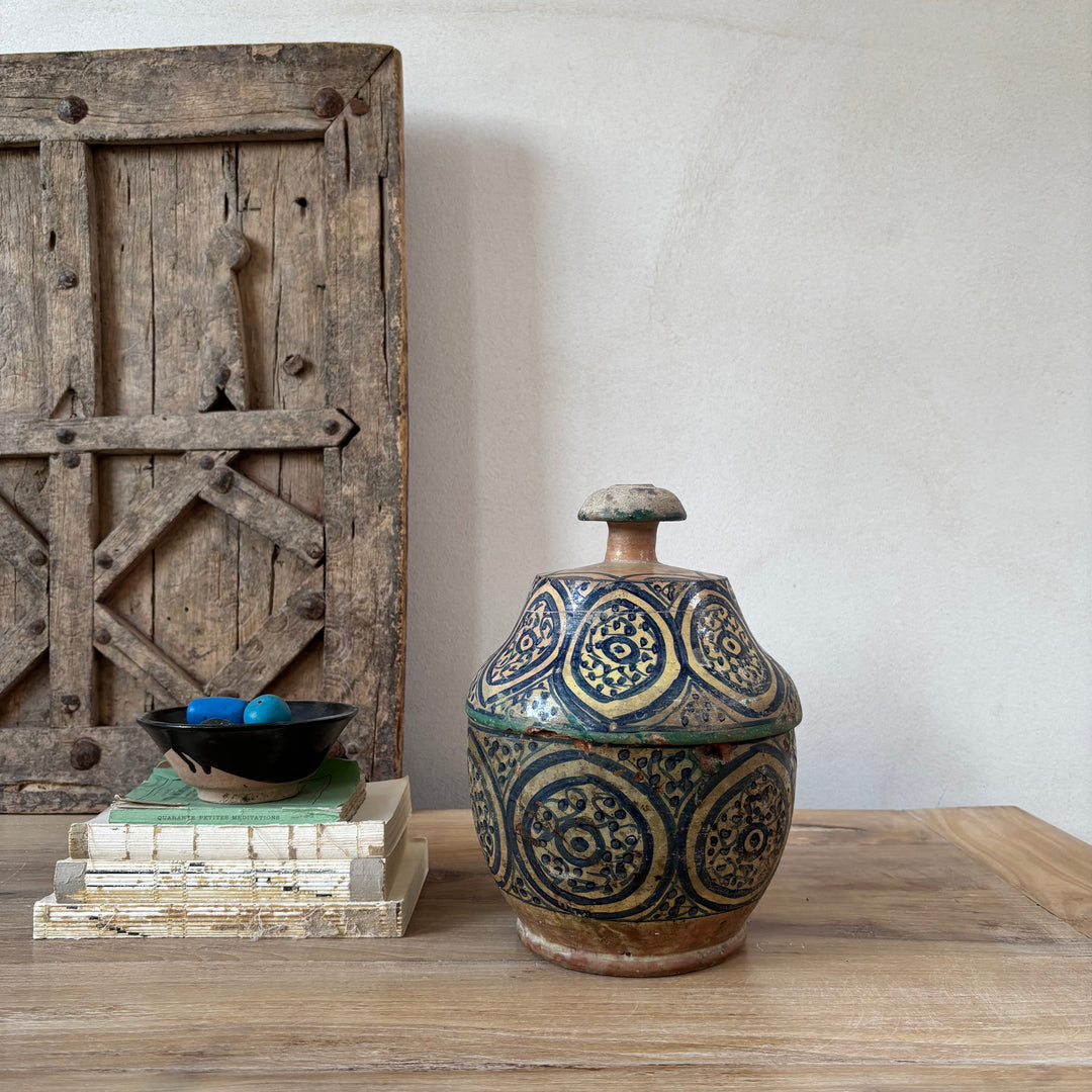 Decorative ceramic jar with intricate patterns on a wooden surface, with a rustic wooden door in the background.