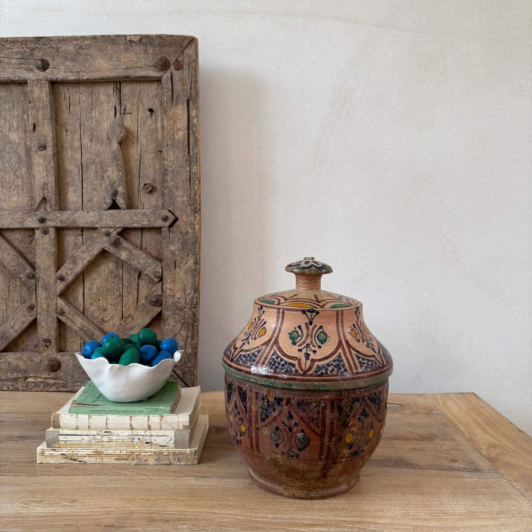 Decorative ceramic jar with intricate patterns on a wooden surface, with a rustic wooden panel in the background.