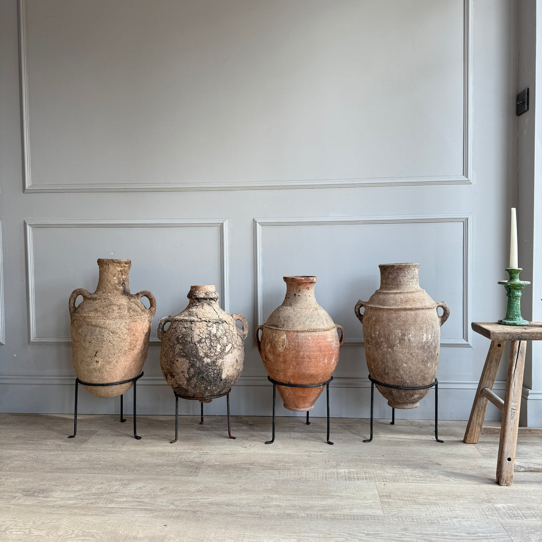 Four large ceramic urns on stands against a gray paneled wall.