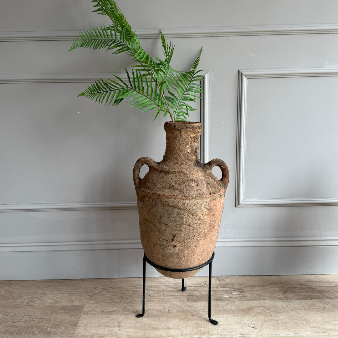 Decorative vase with green plant on a stand against a gray wall