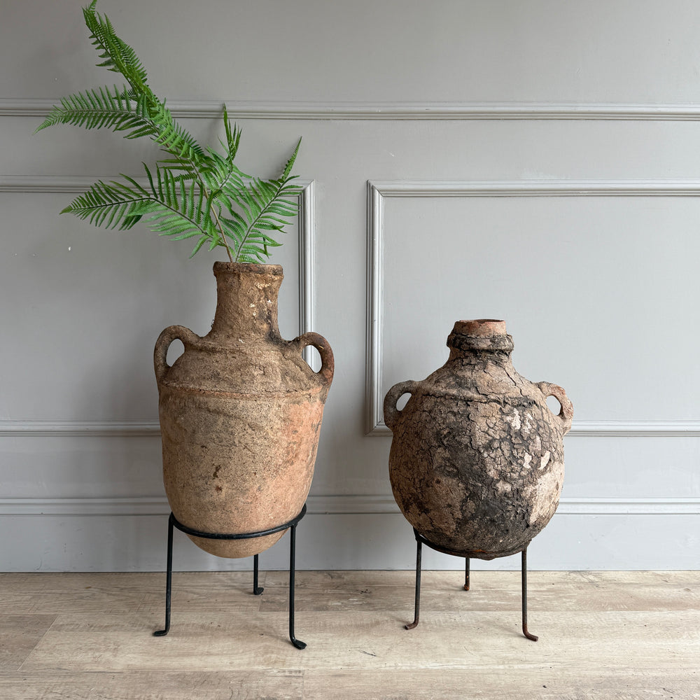 Two rustic clay pots on stands against a neutral wall.