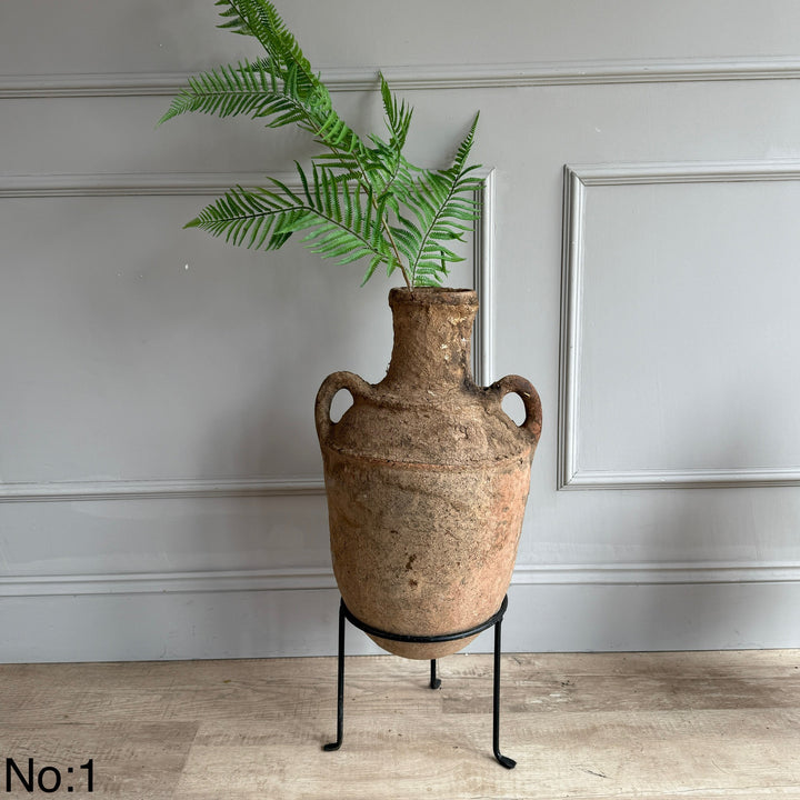 Decorative vase with a plant on a stand against a gray wall