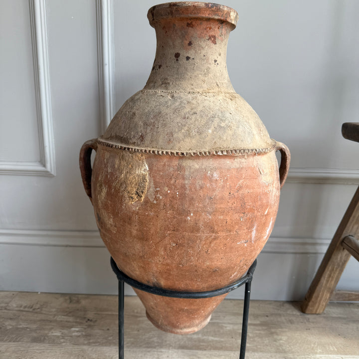Vintage terracotta vase on a stand against a neutral wall.