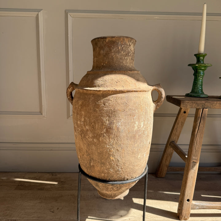 Large brown ceramic vase on a stand in a room with wooden floor and wall.