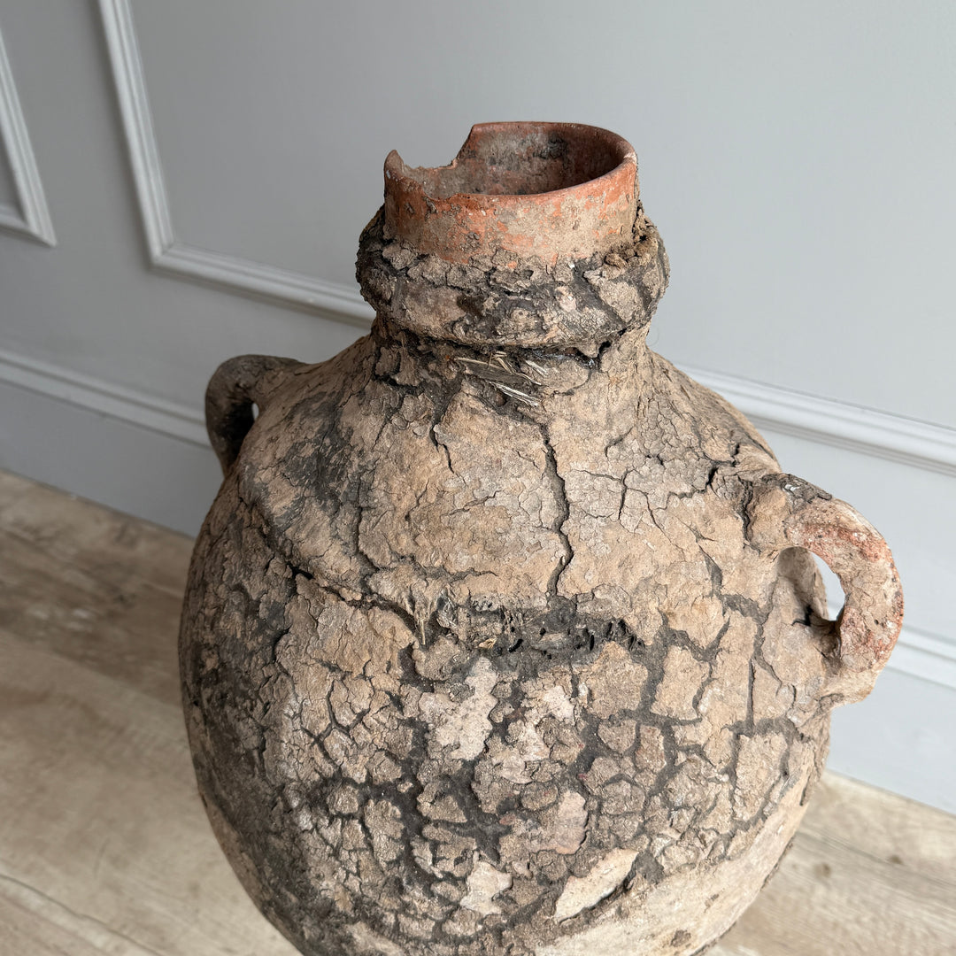 Vintage ceramic jar with cracked surface on a wooden floor against a gray wall.