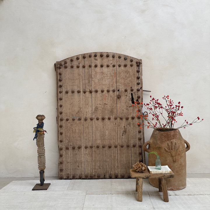 Decorative elements including a large wooden door, vase with flowers, and small table against a plain wall.