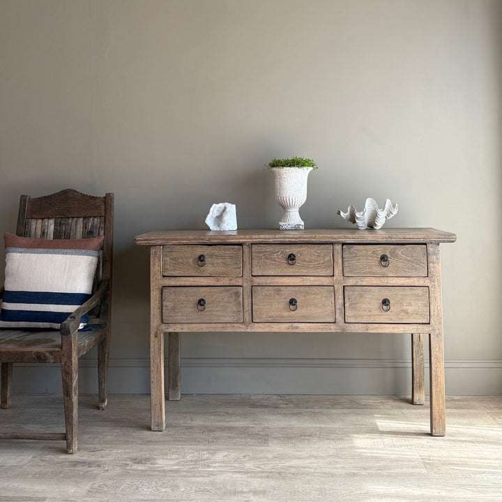 Wooden console table with drawers and decorative items against a plain wall.